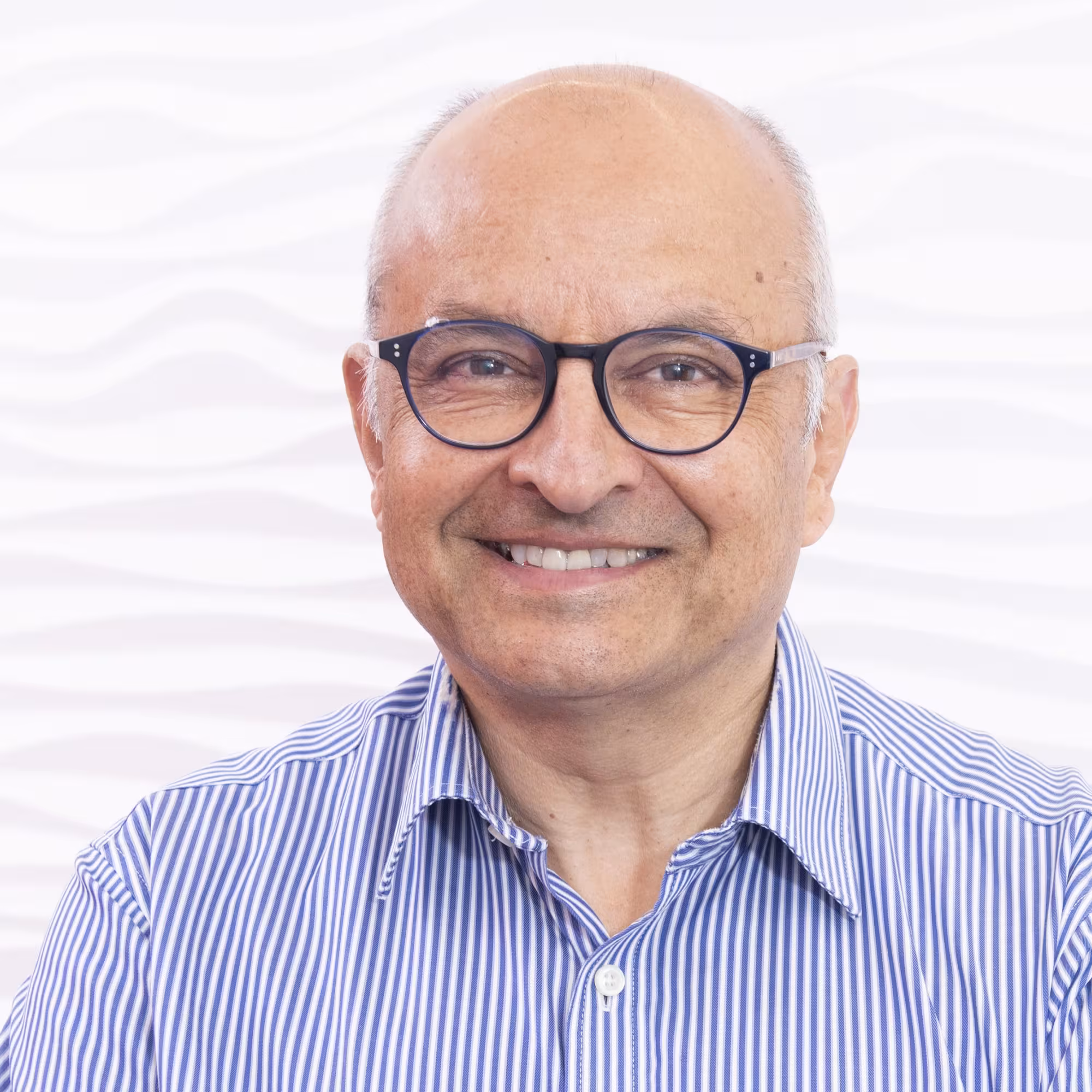 Portrait of Professor Ketan Patel, a man of Asian descent wearing a striped shirt and standing in front of a plain white background.