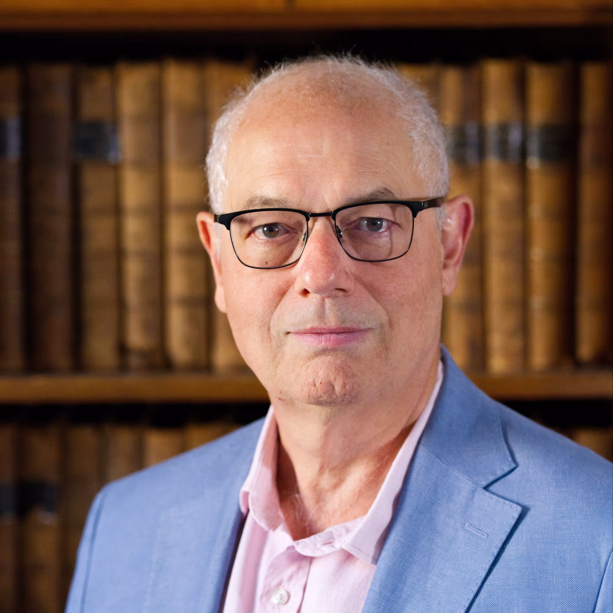 Portrait of Tom Melham, a white man wearing glasses standing in front of a bookcase.