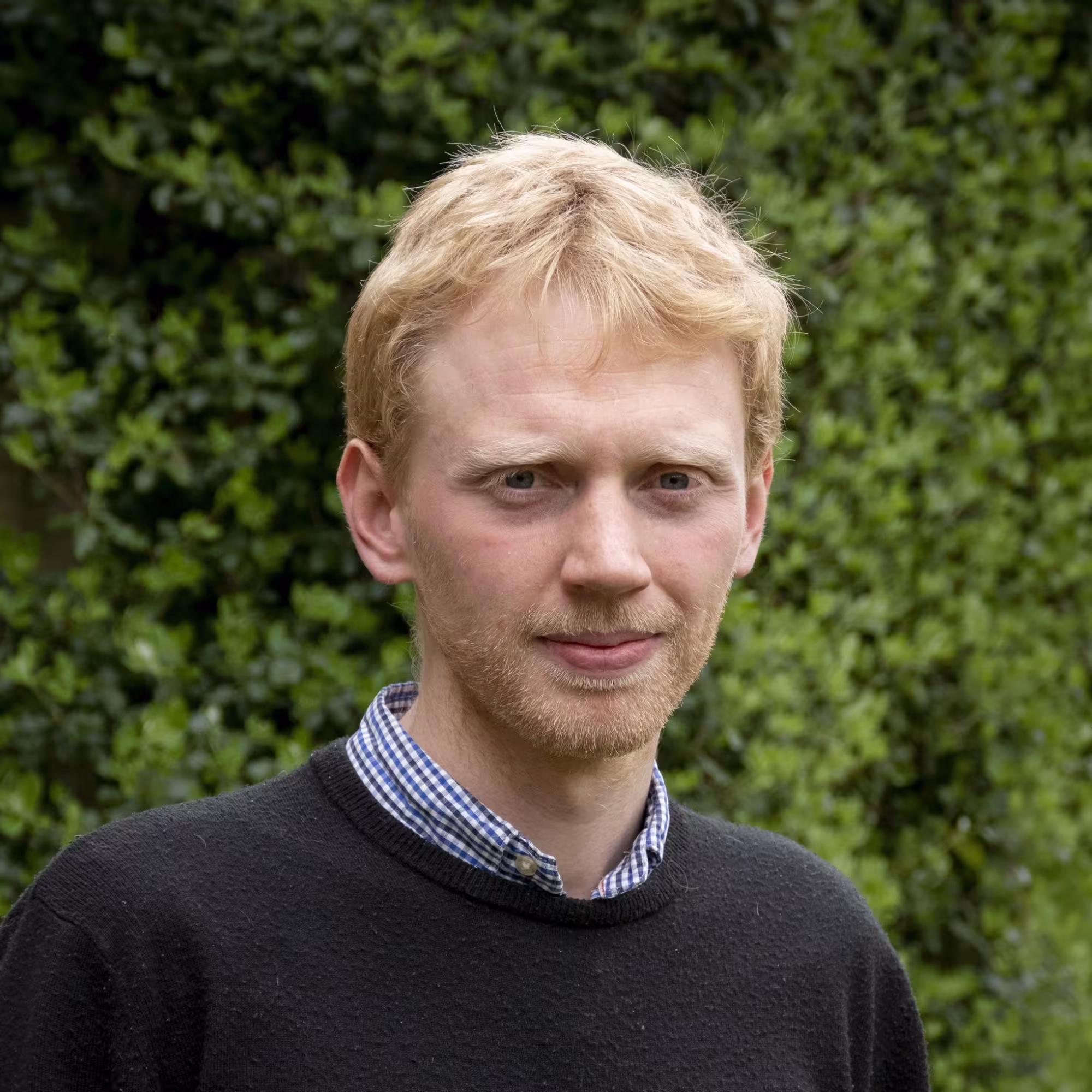 Portrait of James Read, a white man with blonde hair, standing in front of a hedge.