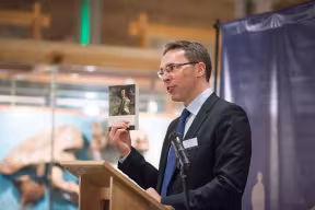 Nigel Portwood standing at a podium holding a book