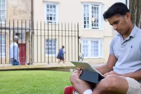 Oxford student with a laptop sat by a tree.