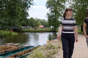 Two students walking past punts on the river