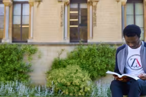 Student sat reading in front of the Museum of Natural History, Oxford.