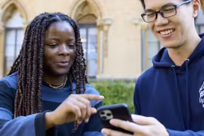 Two people sitting outside, looking at a phone.