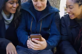 Three students in the grounds of Green Templeton College looking at a mobile.