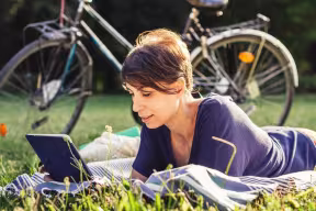 A woman lies on grass reading in front of a bike