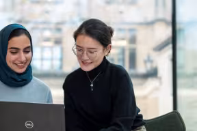 Two students sat side by side looking at a laptop.