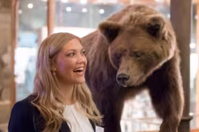 a woman laughing in front of a stuffed bear at a museum