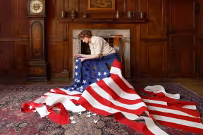 A woman sits on a chair stitching an American flag