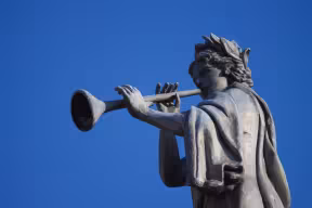 A statue of a muse on top of the Clarendon Building against a blue sky