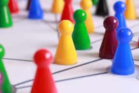 Photo of yellow, green and red pawn figures on a white lined board.