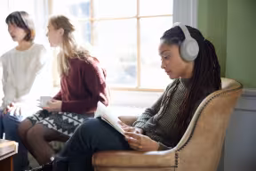 A STUDENT LISTENING TO MUSIC IN COLLEGE SURROUNDED BY OTHERS