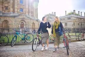 Students walking with bikes outside the Radcliffe Camera