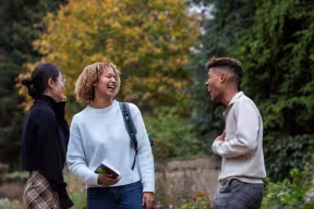 GROUP OF STUDENTS SMILING AND CHATTING IN THE RHODES HOUSE GARDEN