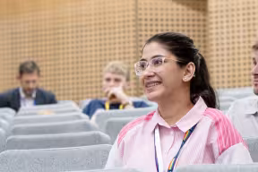 A woman in a pink shirt smiles while sitting in a lecture hall