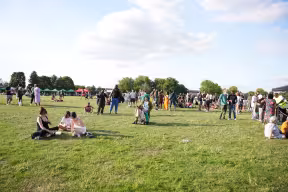 Crowds of people socialising and relaxing at the Leys Festival, gathered across an open green space with pop-up tents and activities behind them.