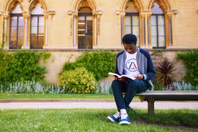 Student reading a book on a bench