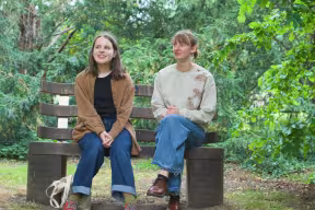 Two students sitting on a bench in woodland