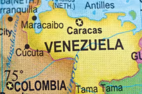 A close‑up of a printed map highlighting Venezuela and surrounding areas, including labeled cities such as Caracas, Maracaibo, and Cúcuta, along with neighboring countries Colombia and Guyana.