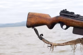 Close-up of a person holding a wooden‑stock rifle near a large body of water