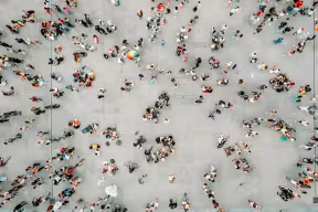 An aerial shot of a crowd of people standing on grey pavement