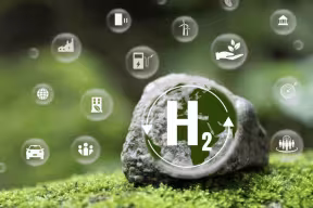 Conceptual image of a rock embedded in green ground with an “H₂” symbol at the center, surrounded by floating icons representing renewable energy, transport, and industry.