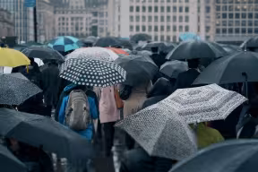 Commuters with umbrellas walking across London Bridge in the heavy rain, with Tower Bridge in the background.