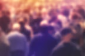 Abstract, blurred image of a large crowd of people viewed from behind, with warm-toned lighting and no individual details visible.
