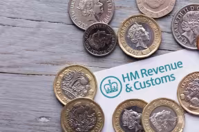 UK coins surrounding an HM Revenue & Customs document on a wooden surface.