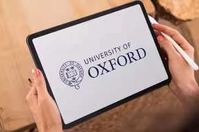 Hands holding a tablet displaying the University of Oxford logo on screen.