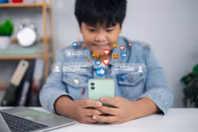 Asian male child using smartphone with social media reaction icons, chatting and online communication concept. 