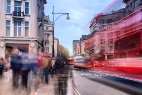 Daytime long exposure on Oxford Street near Oxford Circus on a busy weekend afternoon as shoppers walk past and several buses drive by.