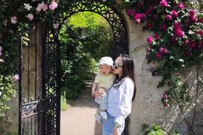 Ling Tao holds her baby in front of a gate in college grounds