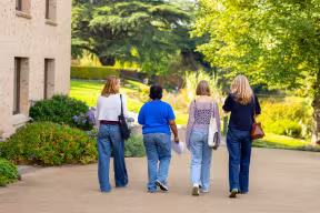 Three Open Day visitors and a student ambassador walking away from camera through a college garden.