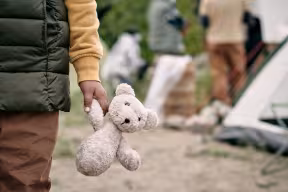Child stands alone with teddy in refugee camp