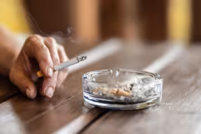 The hand of a smoking woman with a cigarette taps the ash into an ashtray.