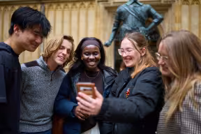STUDENTS LOOKING AT A PHONE TOGETHER IN THE OLD SCHOOLS QUADRANGLE