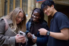 STUDENTS LOOKING AT A PHONE TOGETHER IN THE OLD SCHOOLS QUADRANGLE