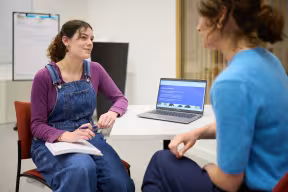 A student sits with a notebook during a one-to-one careers guidance appointment with an adviser. A laptop on the table displays a careers guidance webpage.
