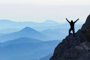 person on mountain side with hands up