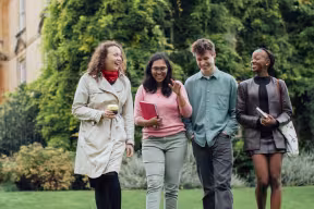 Four students walk together through a garden at the University of Oxford, talking and smiling.