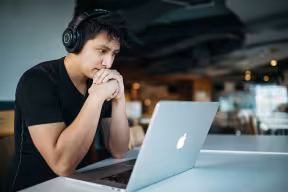 Person with headphones on thinking and looking at laptop