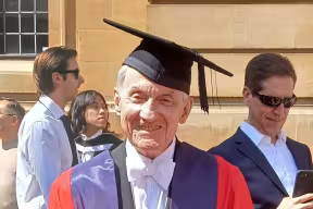 Jeremy Leslie-Spinks in their graduation gown standing outside the Sheldonian theatre
