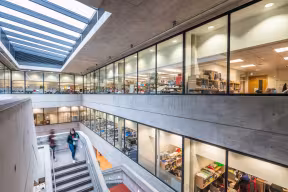 Interior view of a modern research building with exposed concrete walls, glass-walled laboratories and offices spanning multiple floors. 