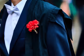 Student wearing a blue gown with red carnation