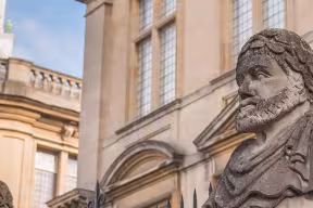 A row of weathered, classical stone bust statues, known as the Emperor Heads, mounted on the railings outside the Sheldonian Theatre in Oxford