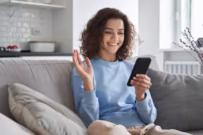 Smiling person waves while talking on mobile phone 