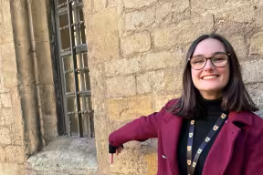 Olivia Butterfield wearing a pink coat, pointing at the Brasenose Lane street sign