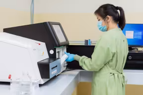An OUCRU researcher loads a prepared DNA library cartridge into an Illumina MiSeq sequencer for genomic analysis