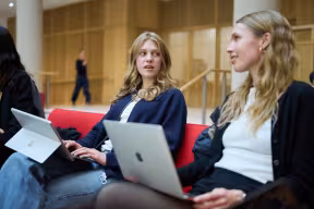 Three students sit together in the Schwarzman Centre with laptops, talking. 